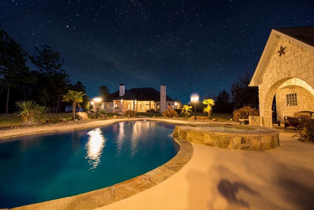 Night view of a lit stone house and pool under a starry sky, Carroll Creek Ranch, Red River County, Texas