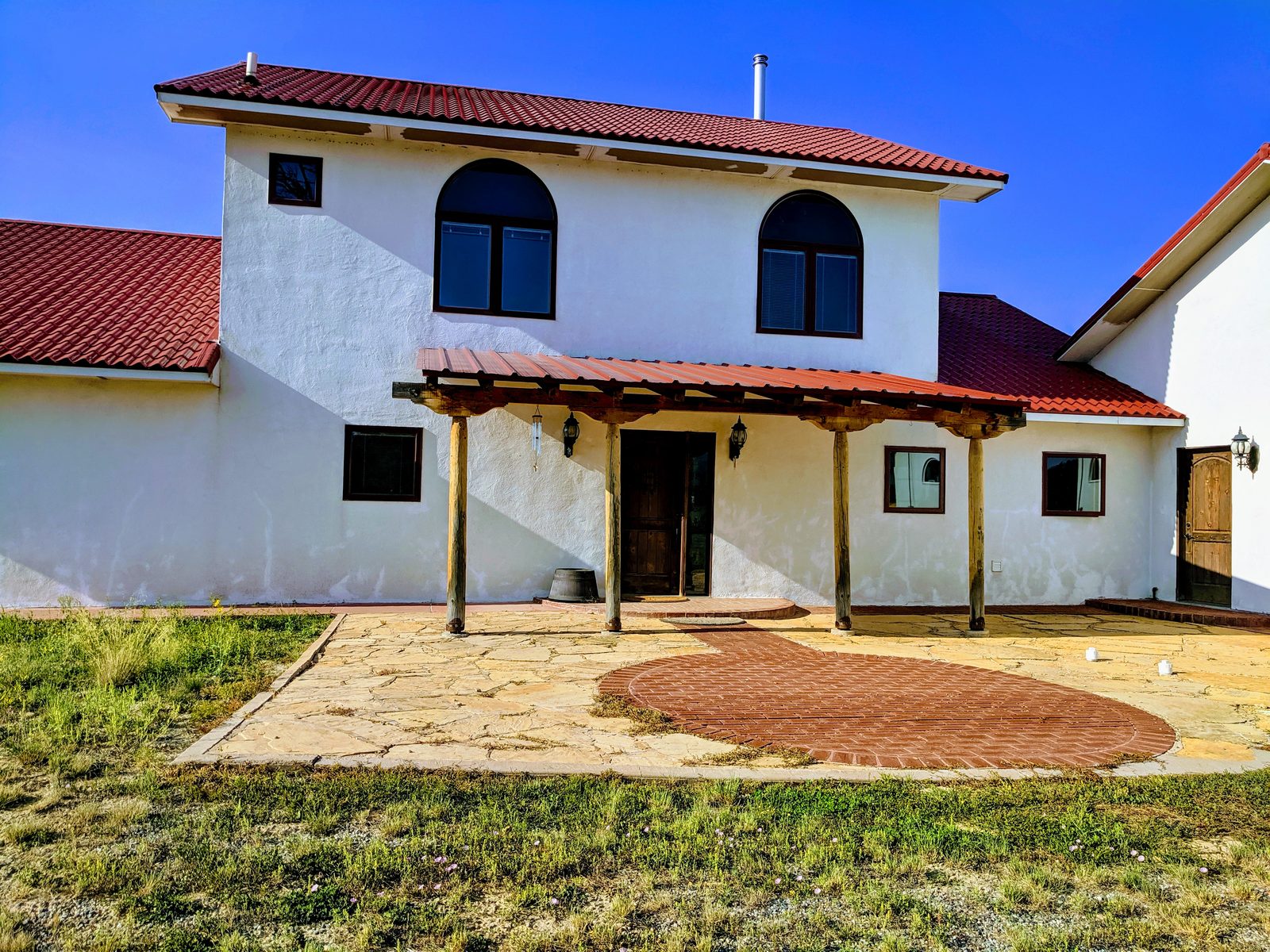 White stucco house with arched windows, wood pergola, and flagstone patio at Casa Blanca, Rio Arriba County, New Mexico