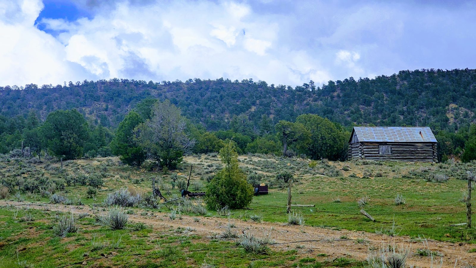 Log cabin at the edge of a meadow below forested hills at Chupadera Ranch, Rio Arriba County, New Mexico