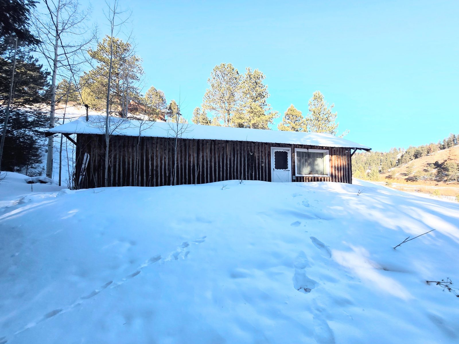 Long wood outbuilding on a snowy rise under blue sky at Foxton Retreat, Jefferson County, Colorado