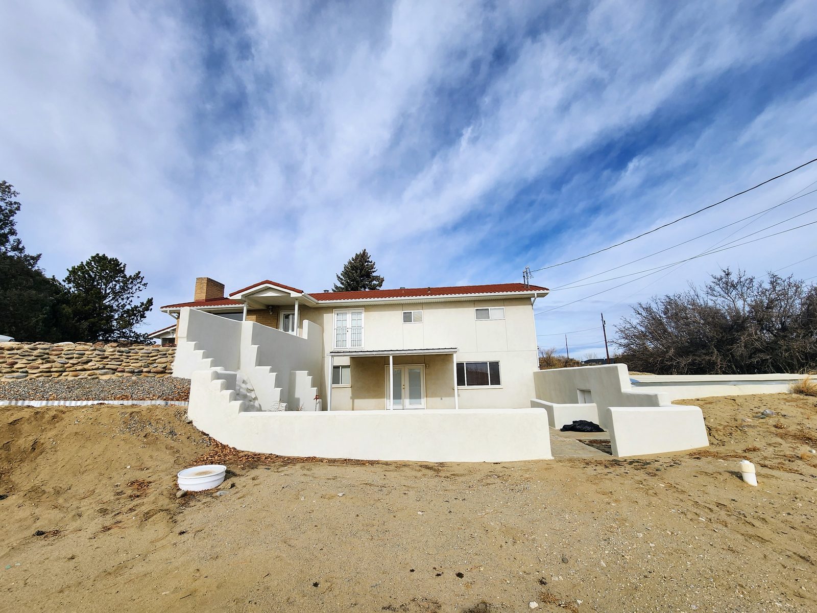 White two-story house on a hillside under a wispy sky at Gomez Farm, San Juan County, New Mexico