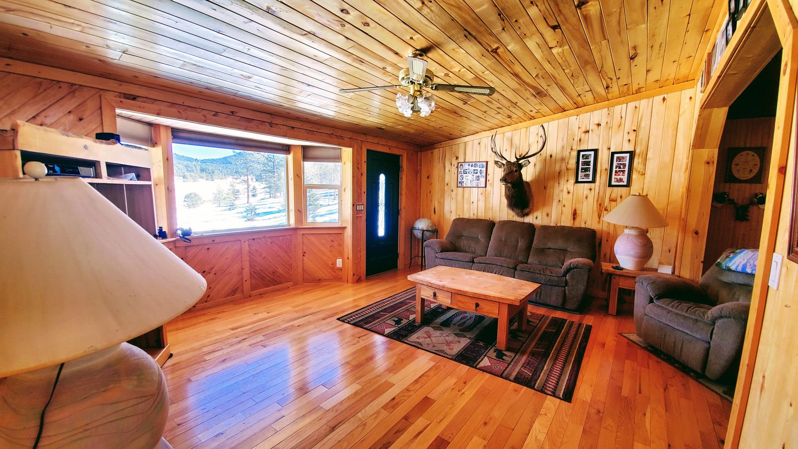 Living room with wood-paneled walls, hardwood floors, and a picture window at Horse Creek Ranch, Lake George, Teller County, Colorado