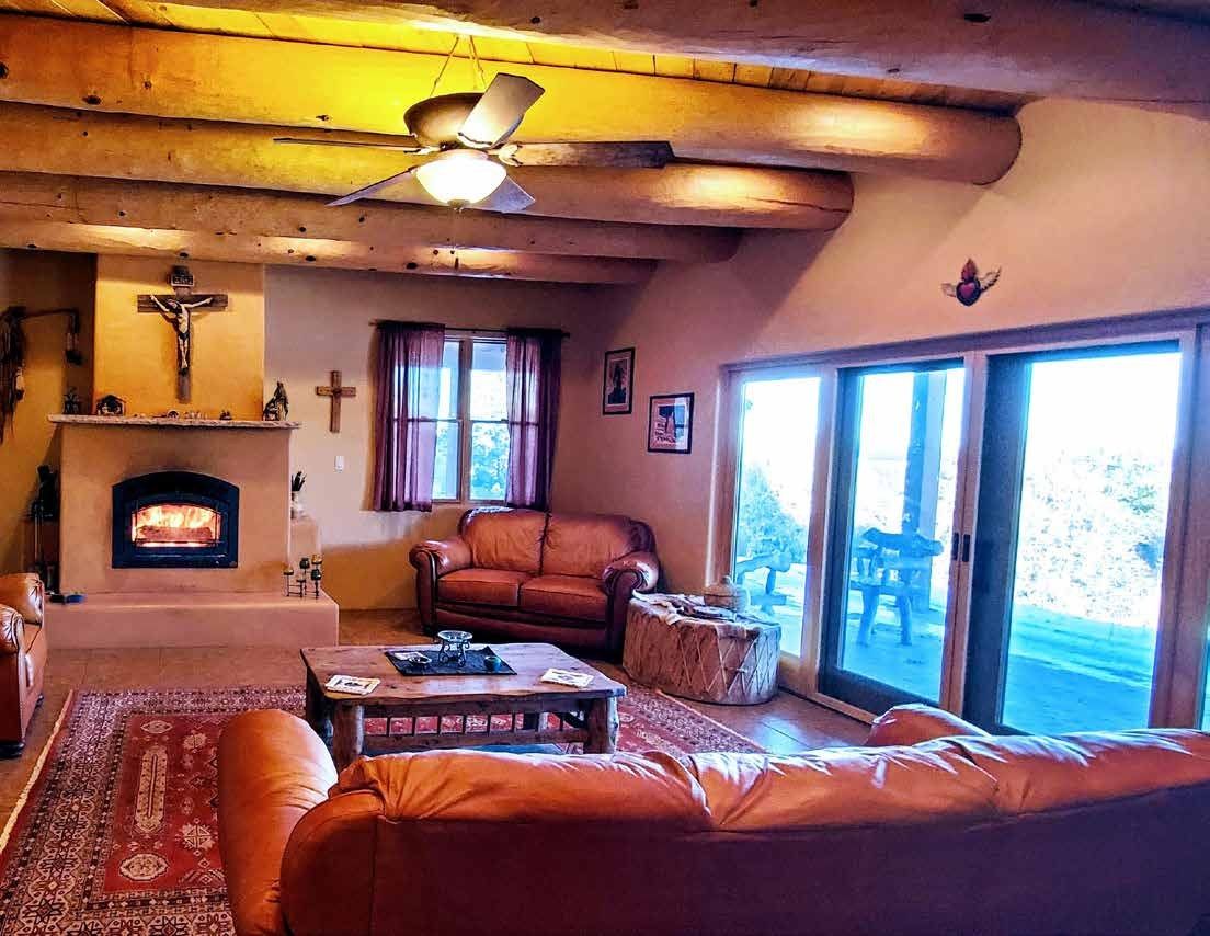 Living room with a fireplace and log ceiling beams at Los Piñones Ranch, Rio Arriba County, New Mexico
