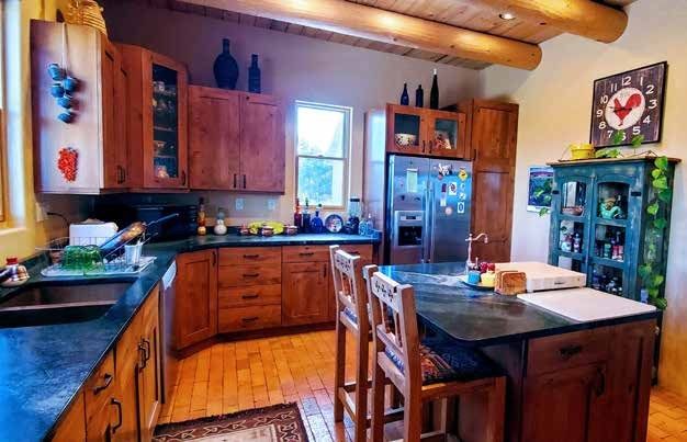 Kitchen with wood cabinets and log ceiling beams at Los Piñones Ranch, Rio Arriba County, New Mexico