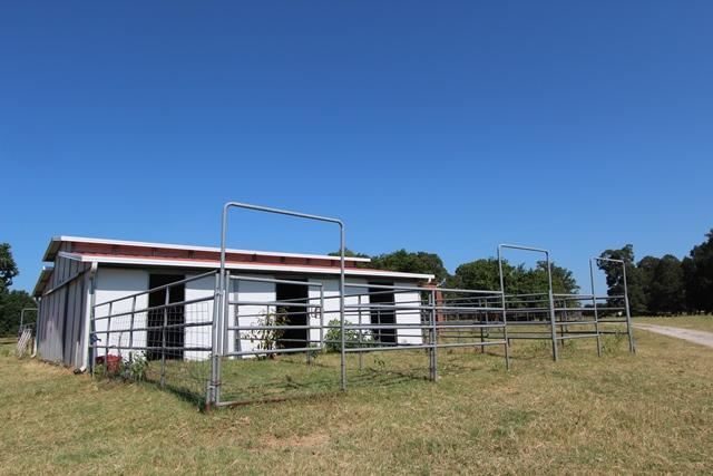 Log house with a covered porch and a green lawn at Pine Creek Ranch, Red River County, Texas