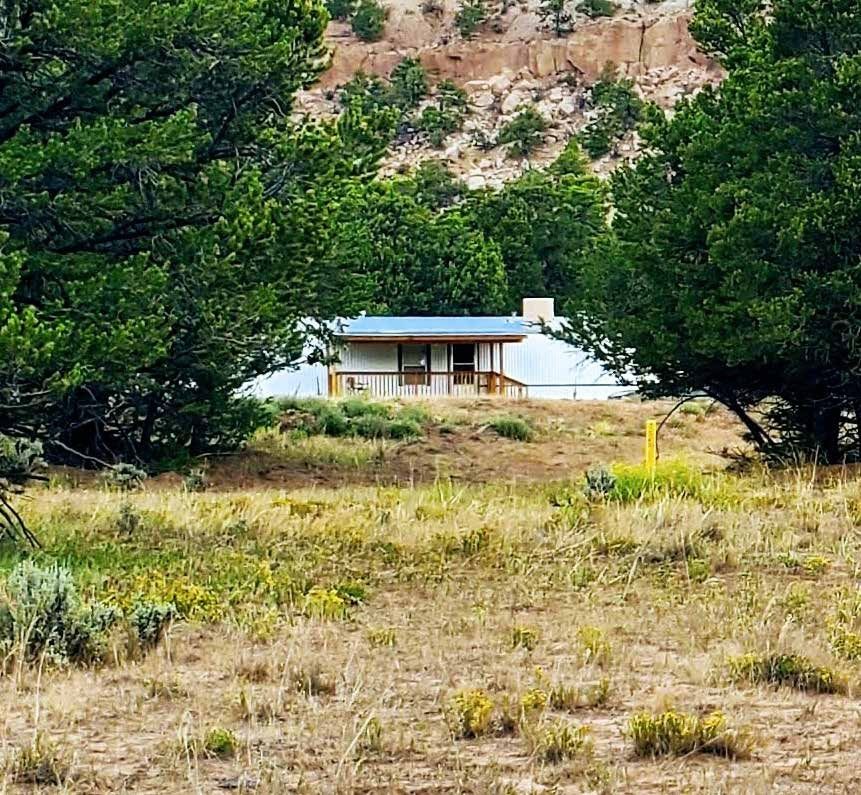 House with a metal roof among pines below a rocky cliff at Secret Valley Ranch, Rio Arriba County, New Mexico